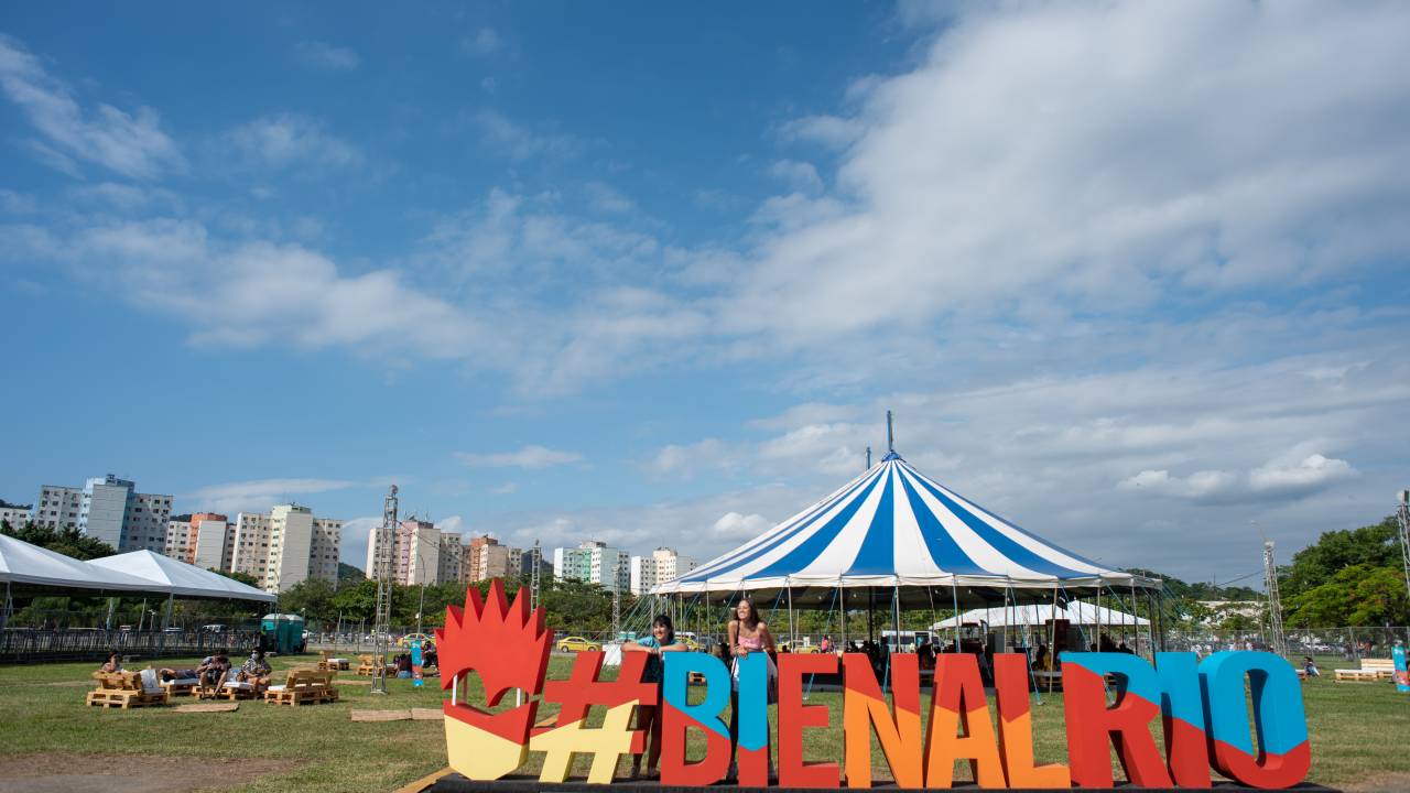 Jardim do Riocentro, com tenda de circo e o letreiro colorido #Bienal em primeiro plano