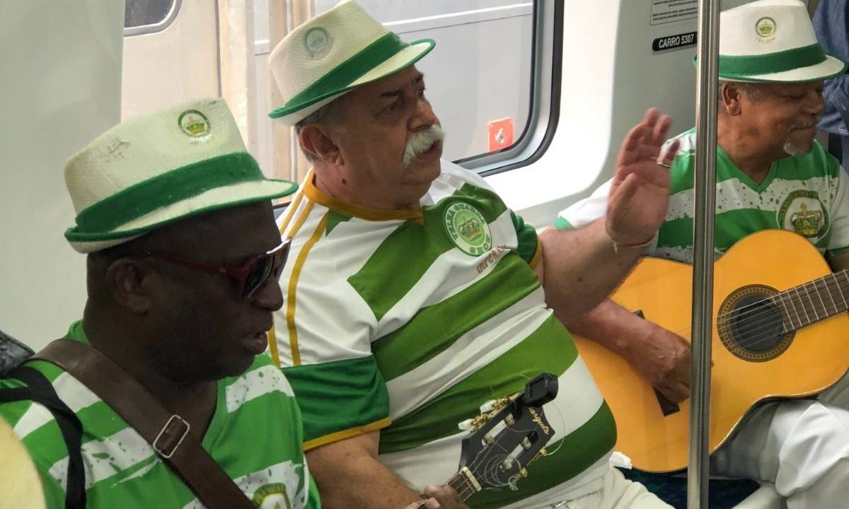 Três homens de chapéu e blusa listrada de verde e banco estão sentados no Trem do Choro