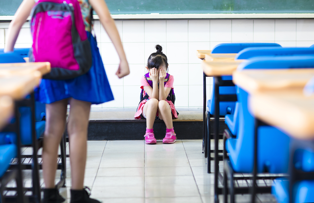 Menina leva as mãos ao rosto em sala de aula.