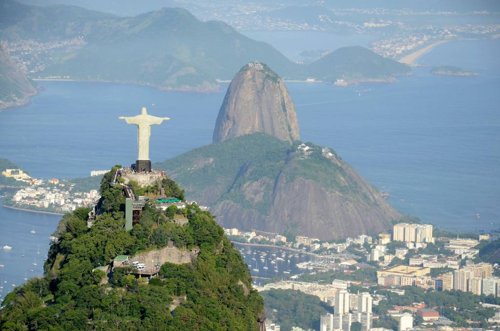 Foto mostra vista aérea do Rio de Janeiro com o Morro do Corcovado em primeiro plano e o Pão de Açúcar ao fundo