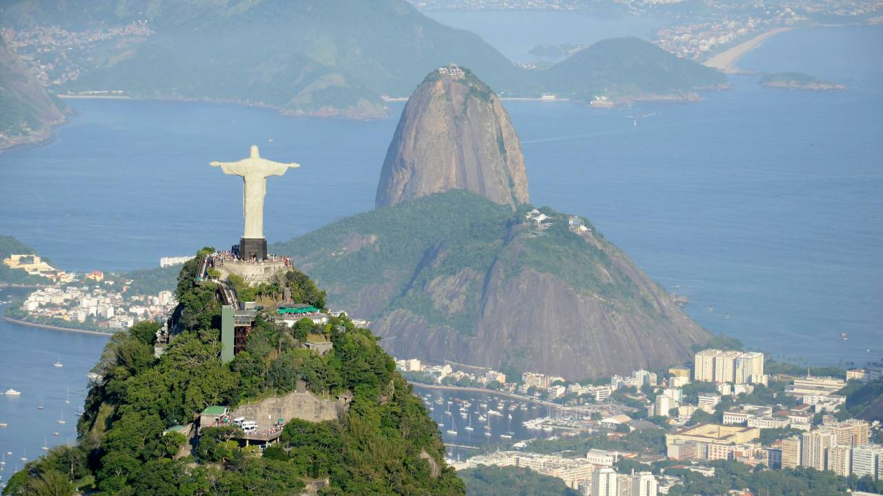 Foto mostra vista aérea do Rio de Janeiro com o Morro do Corcovado em primeiro plano e o Pão de Açúcar ao fundo