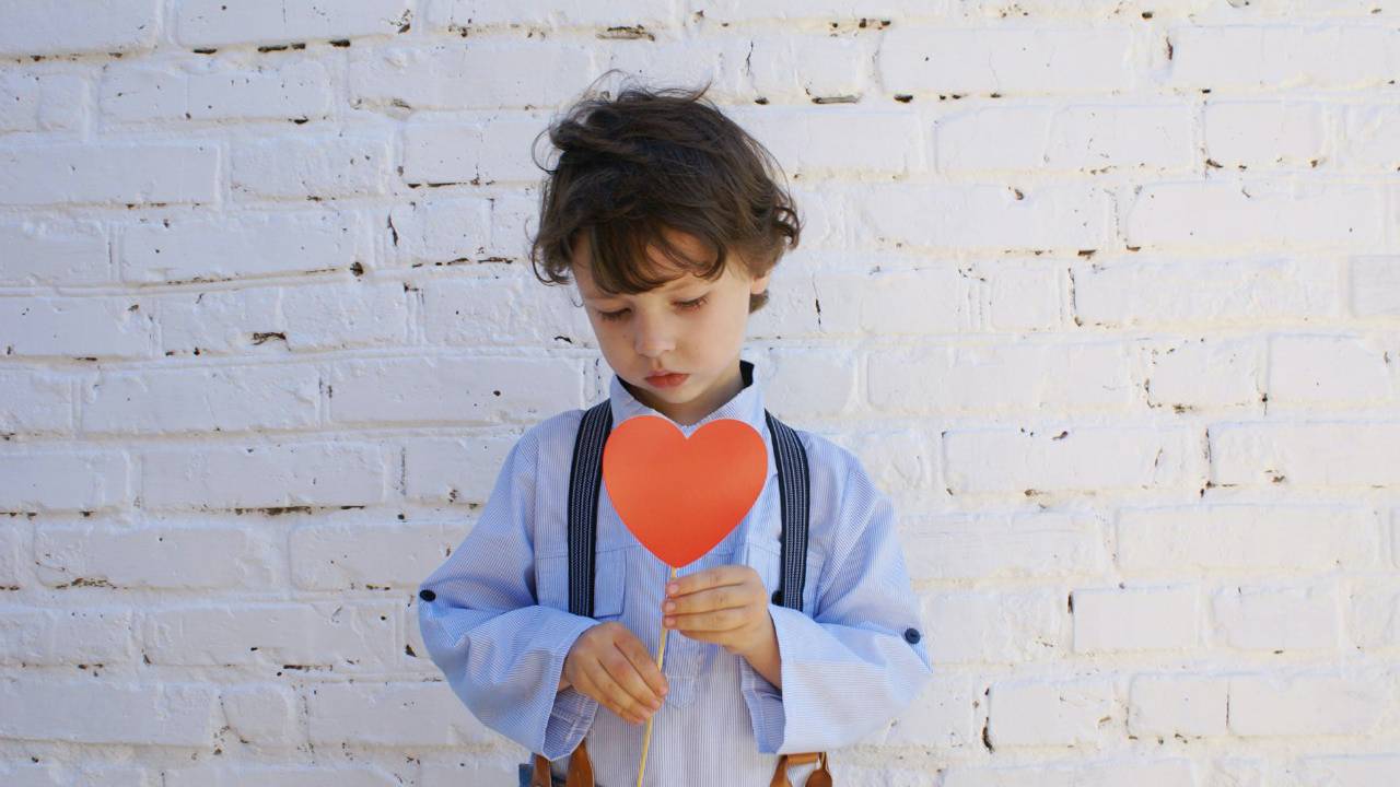Criança triste olhando para um coração de papel.