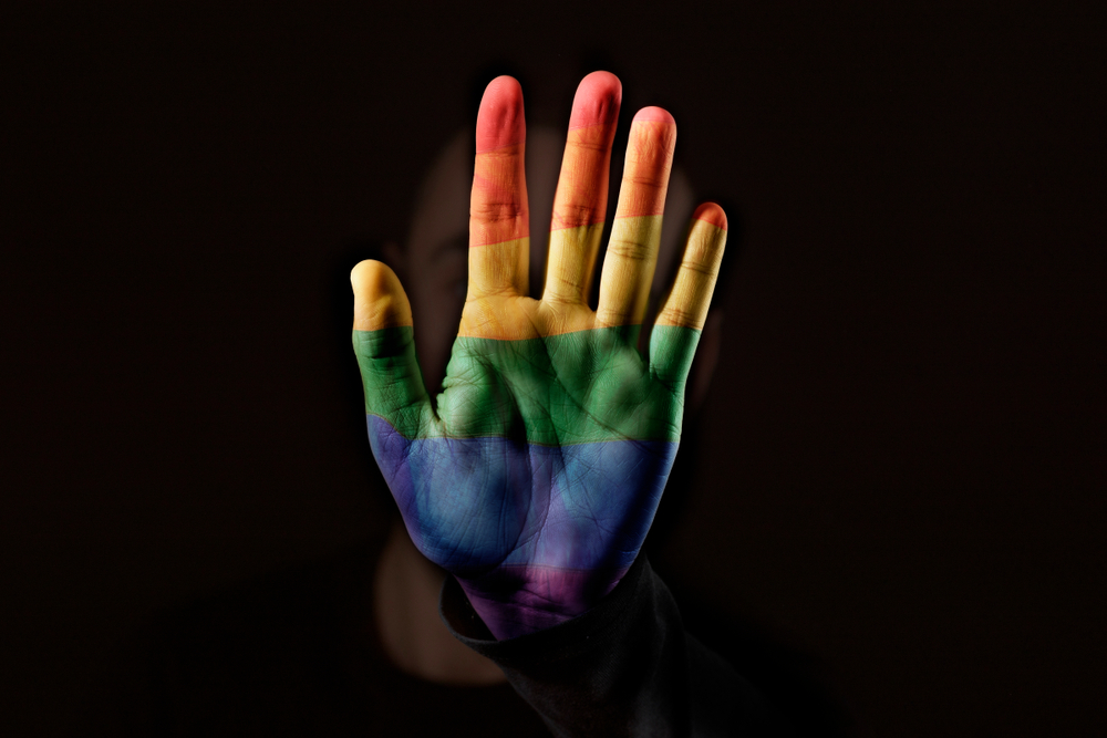 Uma mão em primeiro plano pintada com as cores da bandeira do arco-íris.