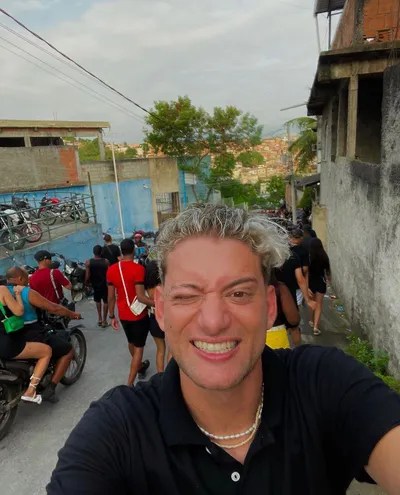 Foto mostra youtuber com cabelo pintado de loiro fazendo selfie em favela carioca