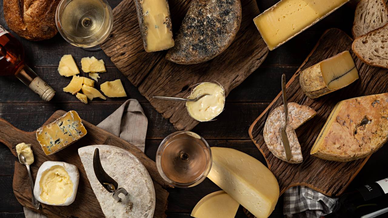 Mesa com diversos queijos, duas taças cheias e uma garrafa de vinho, fotografada de cima