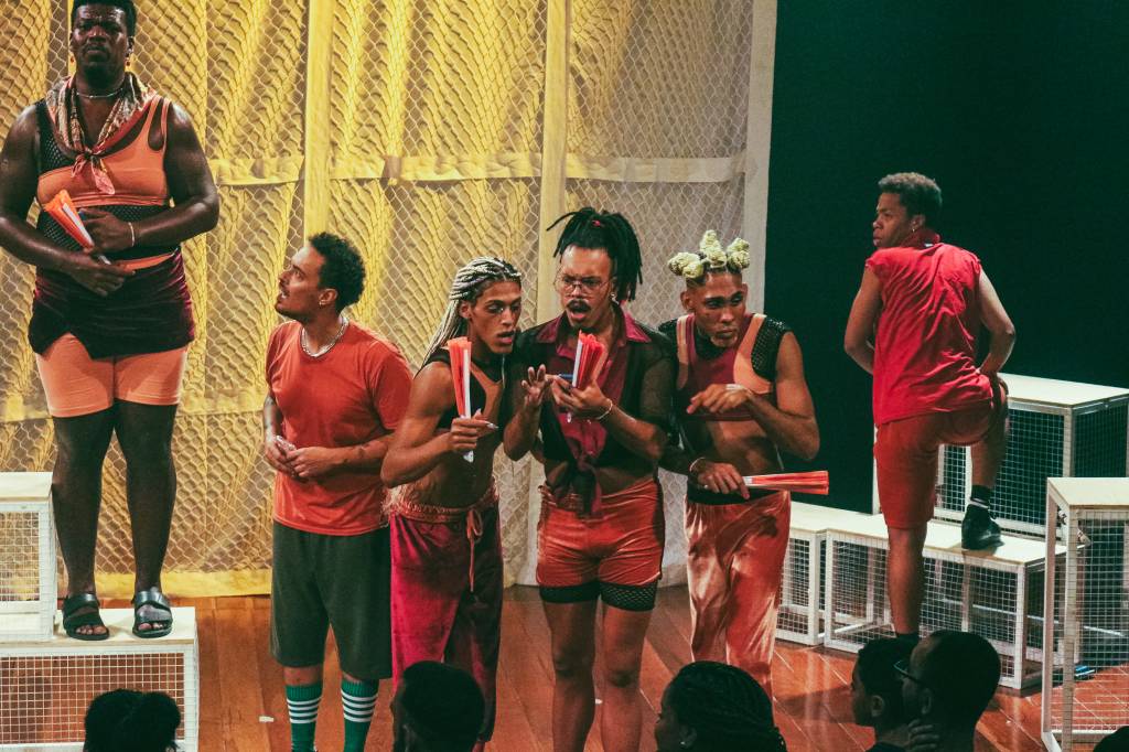 PELADA – A HORA DA GAYMADA A foto mostra seius atores negros com figurino predominantemente vermelho no palco