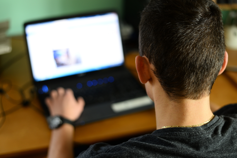 Menino adolescente diante de uma tela de computador.