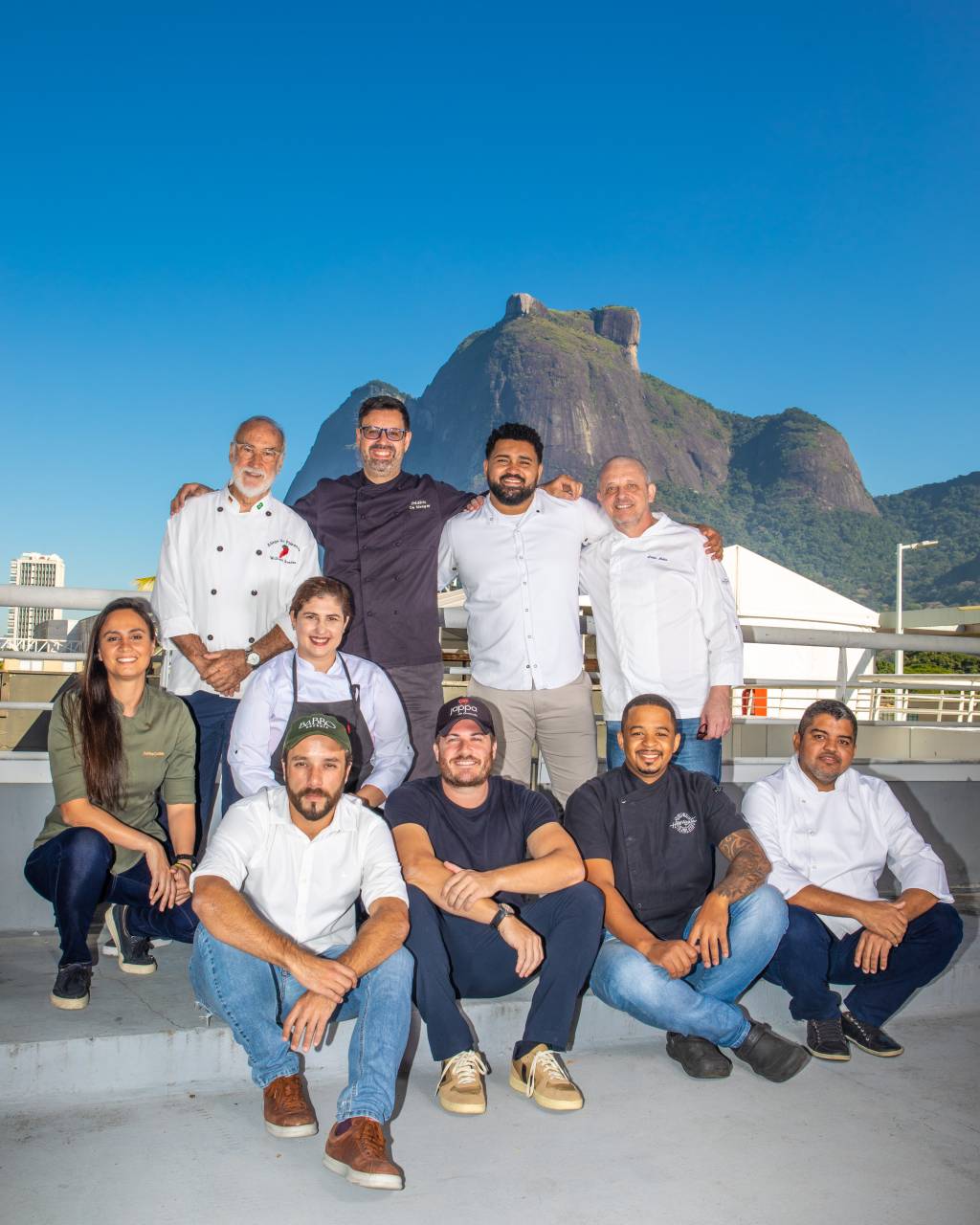 Foto mostra chefs de restaurantes posicionados juntos em terraço, com a Pedra da Gávea ao fundo