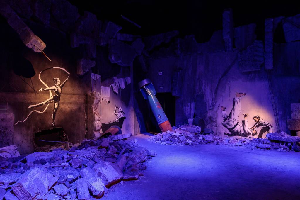 banksy-kahlo-30012023-rfonseca-008 Cenário com luz roxa e um míssil no canto esquerdo reproduz um local bombardeado e traz estêncil de Bansky na parede