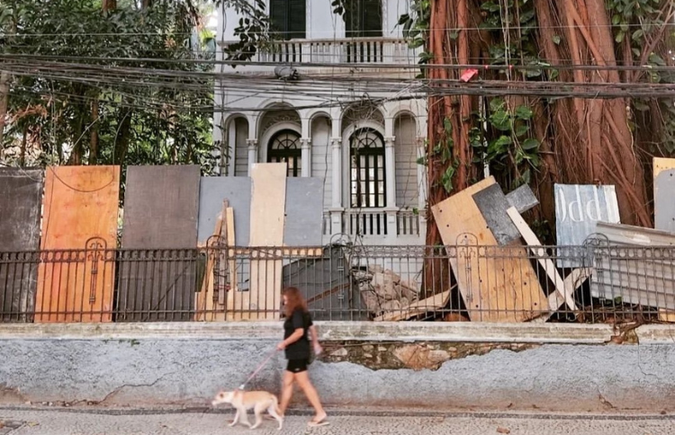 Mulher passeia com seu cão em frente a uma casa abandonada e antiga