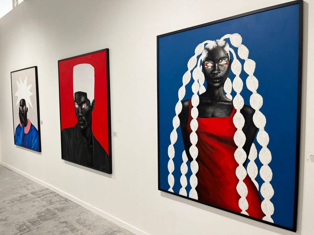 À esquerda, uma tela quadrada de um homem negro com corte de cabelo flat top branco, sobre fundo vermelho. à direita, uma mulher negra de vestido vermelho, com cabelo com tranças.