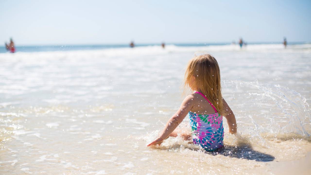 criança sentada na areia da praia, em dia ensolarado