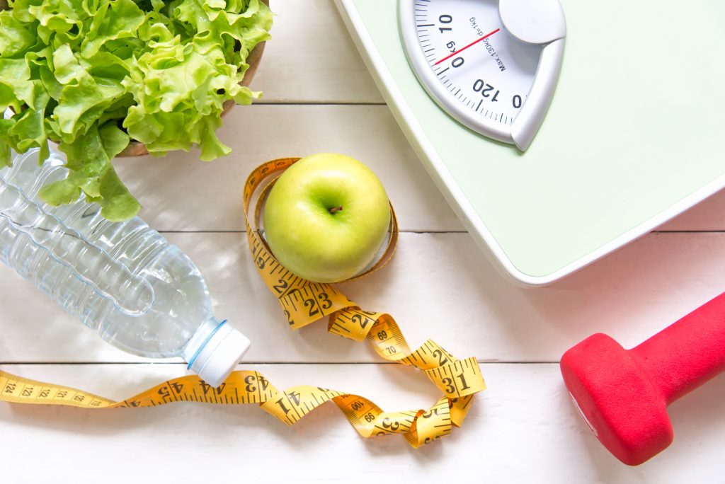 Elementos associados à saúde como balança, maçã, alface e fita métrica.