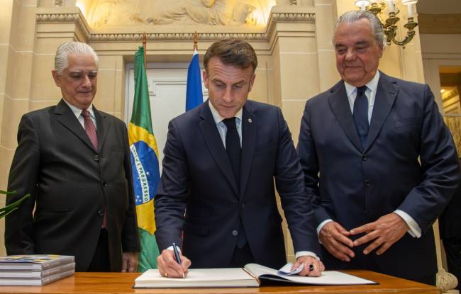Macron assinando o livro de ouro da Casa Firjan, entre o presidente da Firjan, Luiz Césio Caetano, e o presidente do Conselho Superior de Representantes da federação, Eduardo Eugenio Gouvêa Vieira