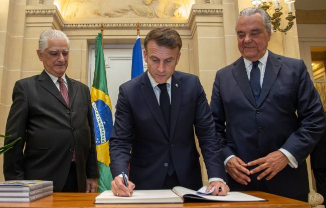 Macron assinando o livro de ouro da Casa Firjan, entre o presidente da Firjan, Luiz Césio Caetano, e o presidente do Conselho Superior de Representantes da federação, Eduardo Eugenio Gouvêa Vieira