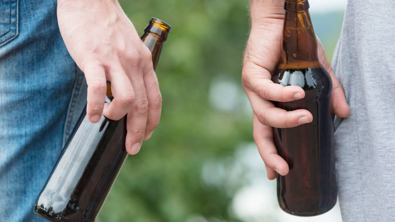 Dois homens seguram garras long neck de cerveja.