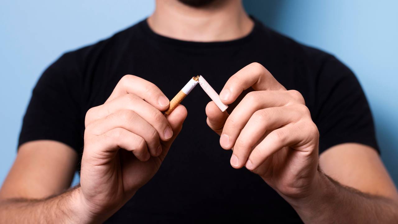 Homem quebra um cigarro em dois pedaços.
