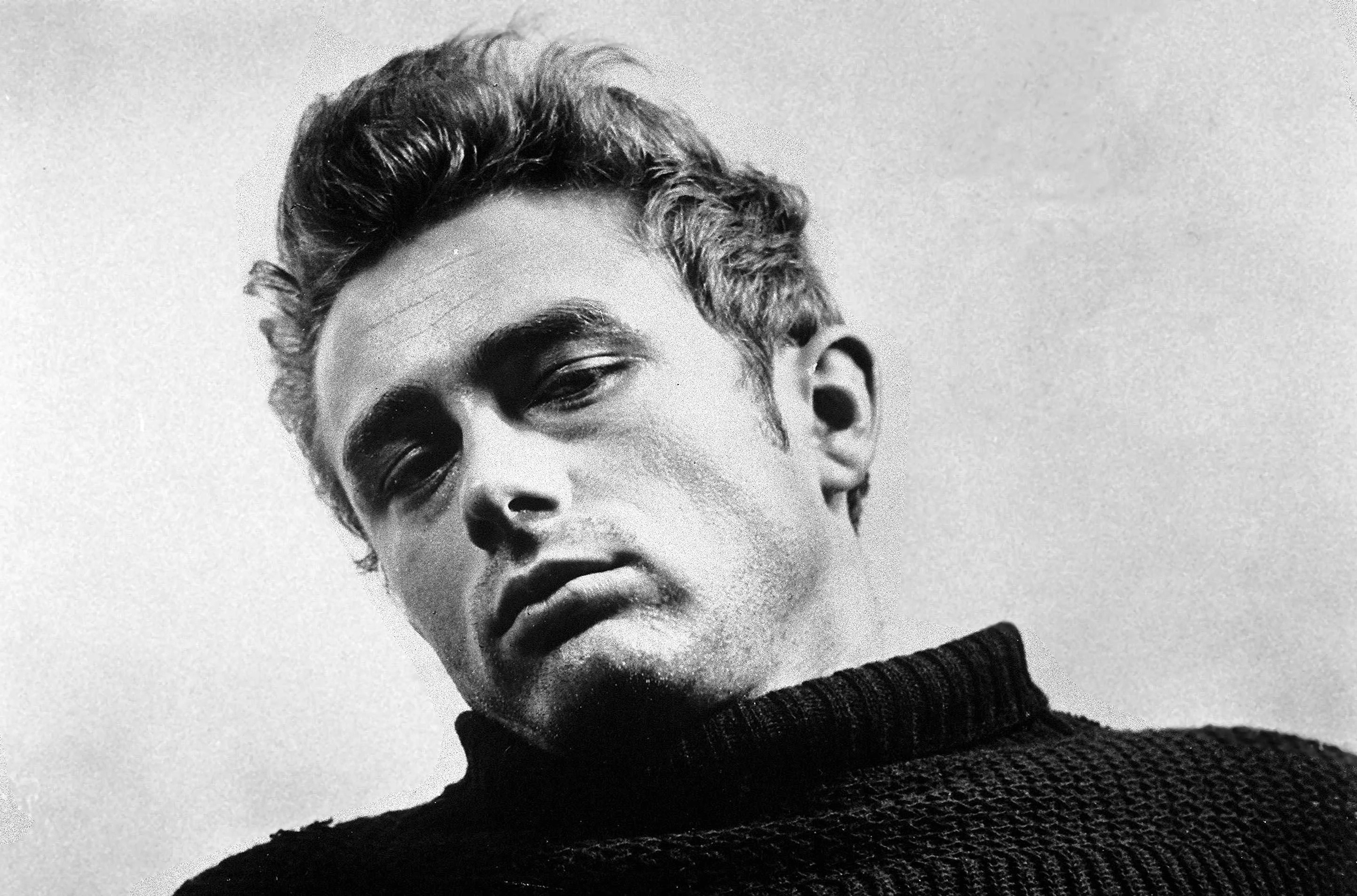 Retrato em preto e branco de um homem jovem, com cabelo escuro e volumoso, olhando para baixo com expressão séria. Ele veste uma blusa de gola alta escura, e a imagem é cortada no ombro.