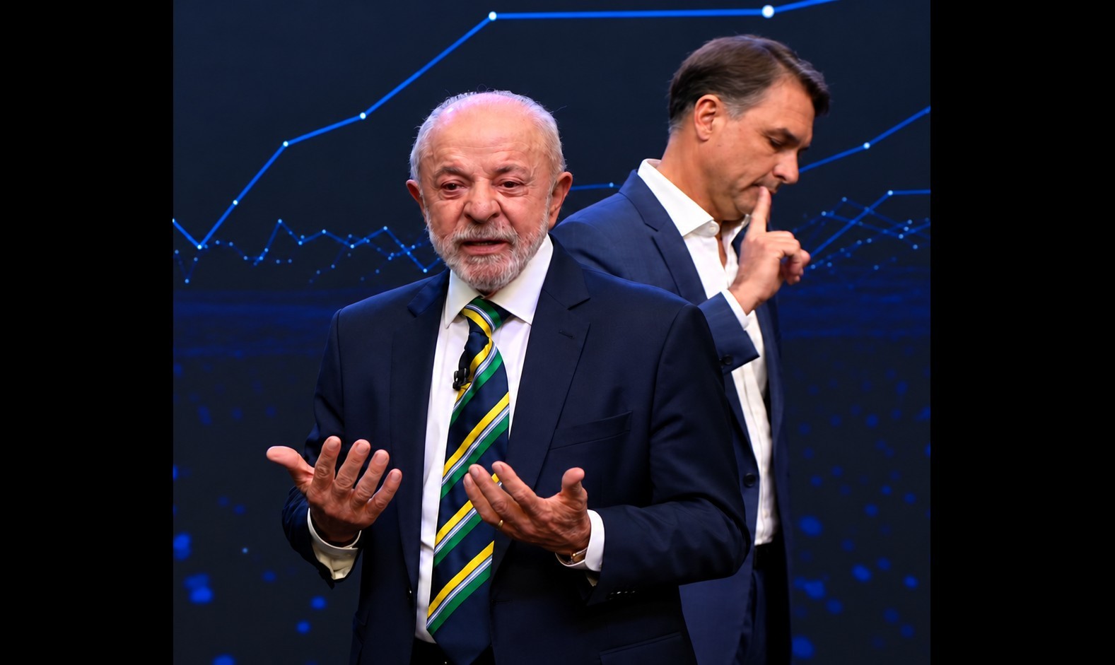 Lula, de terno azul-marinho e gravata verde-amarela, gesticula com as mãos abertas, olhando para frente. Bolsonaro, de terno azul e camisa branca, está atrás e à direita, com a cabeça baixa e o dedo indicador na boca, em um fundo azul escuro com linhas e pontos luminosos que simulam um gráfico